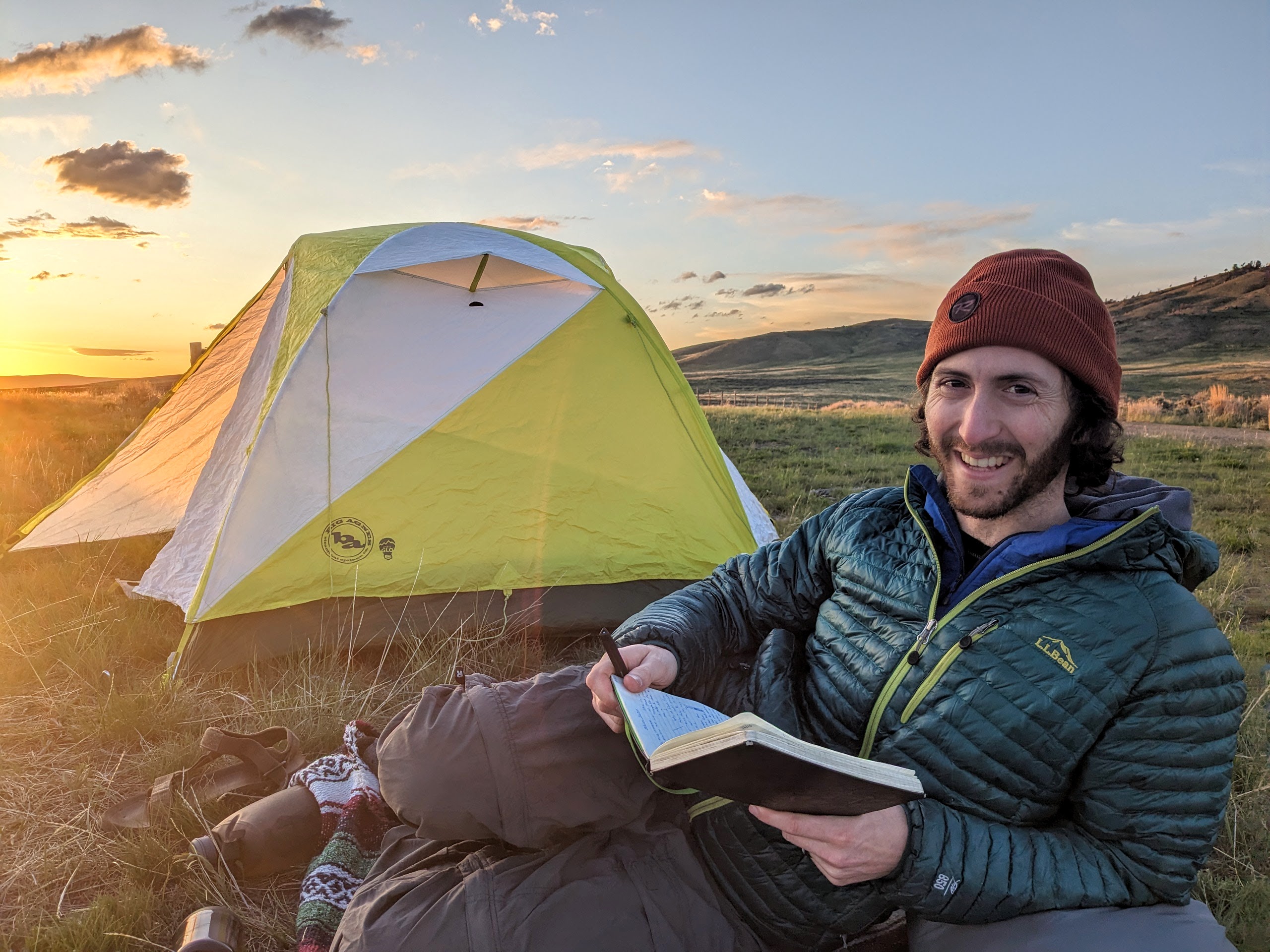 Benya sitting by a tent with a notebook at sunset