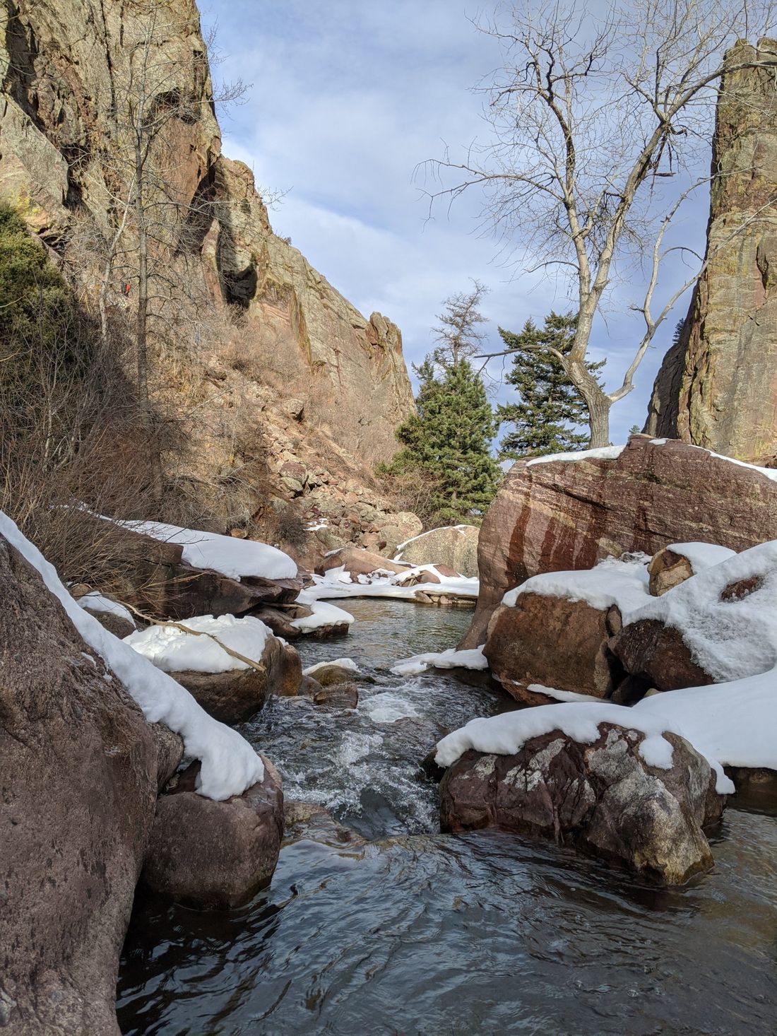 A snowmelt creek running between snow-capped red boulders in a foothills canyon under a winter sky